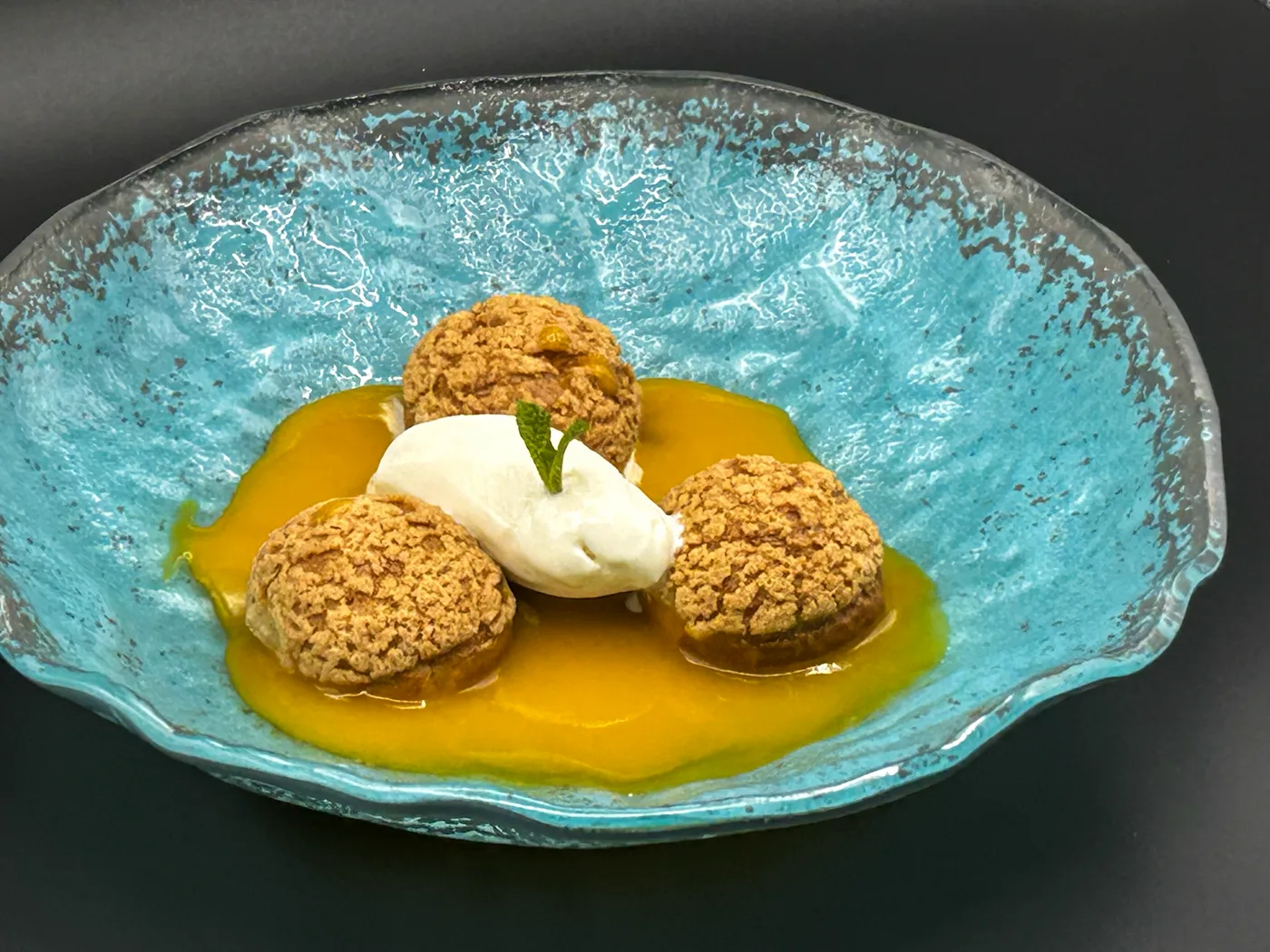 Buñuelos con crema sobre salsa de fruta, en cuenco turquesa